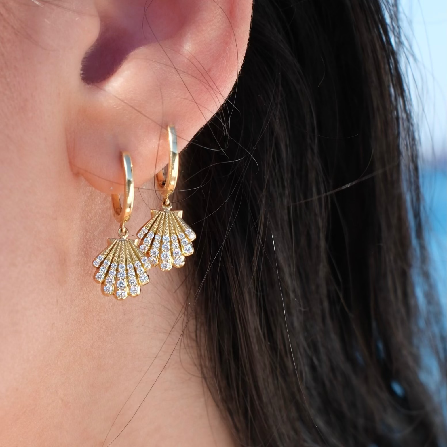 Gold hoop earrings with fan-shaped diamond drops worn by a person.