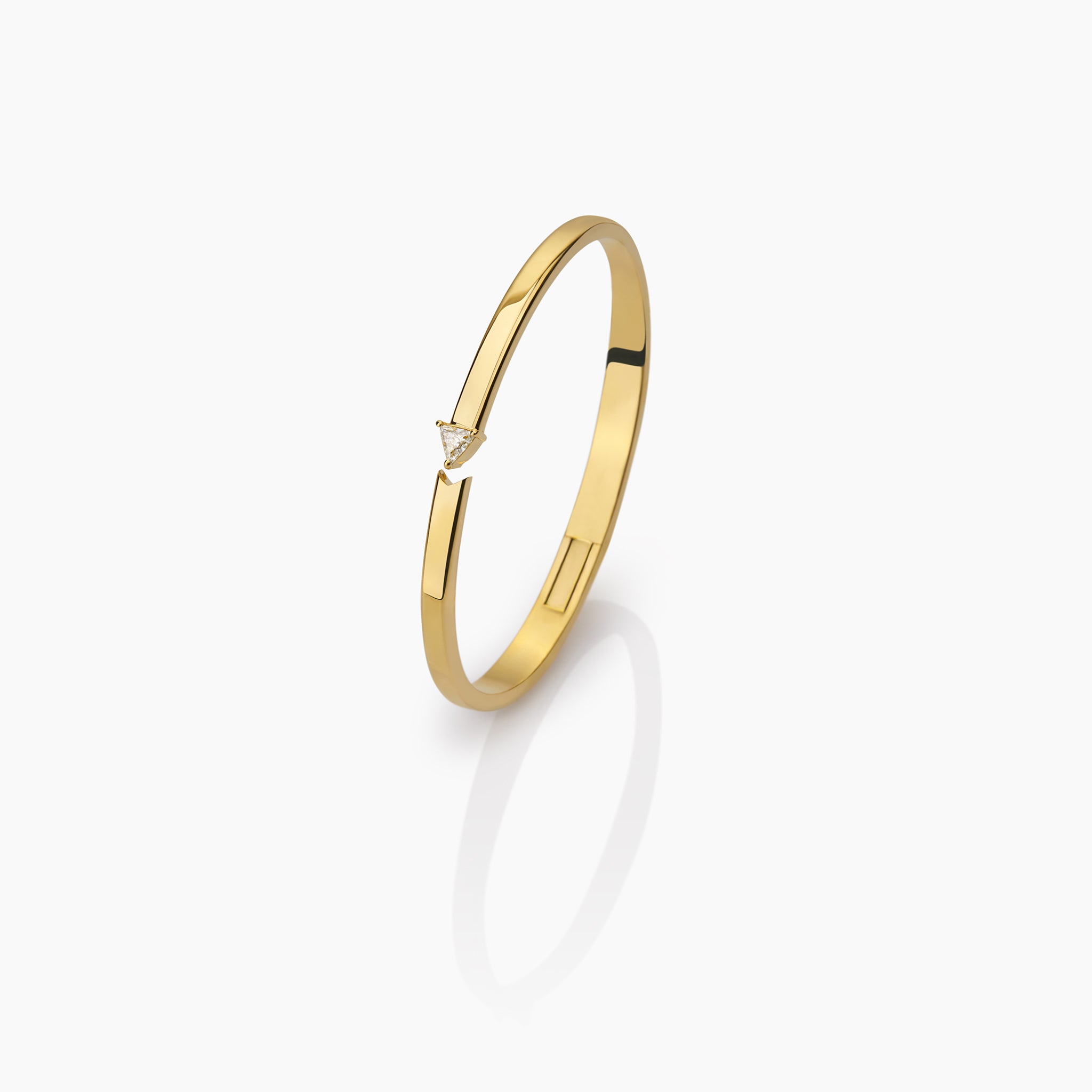 yellow gold bangle with round brilliant diamonds and trillion displayed against an off white background.