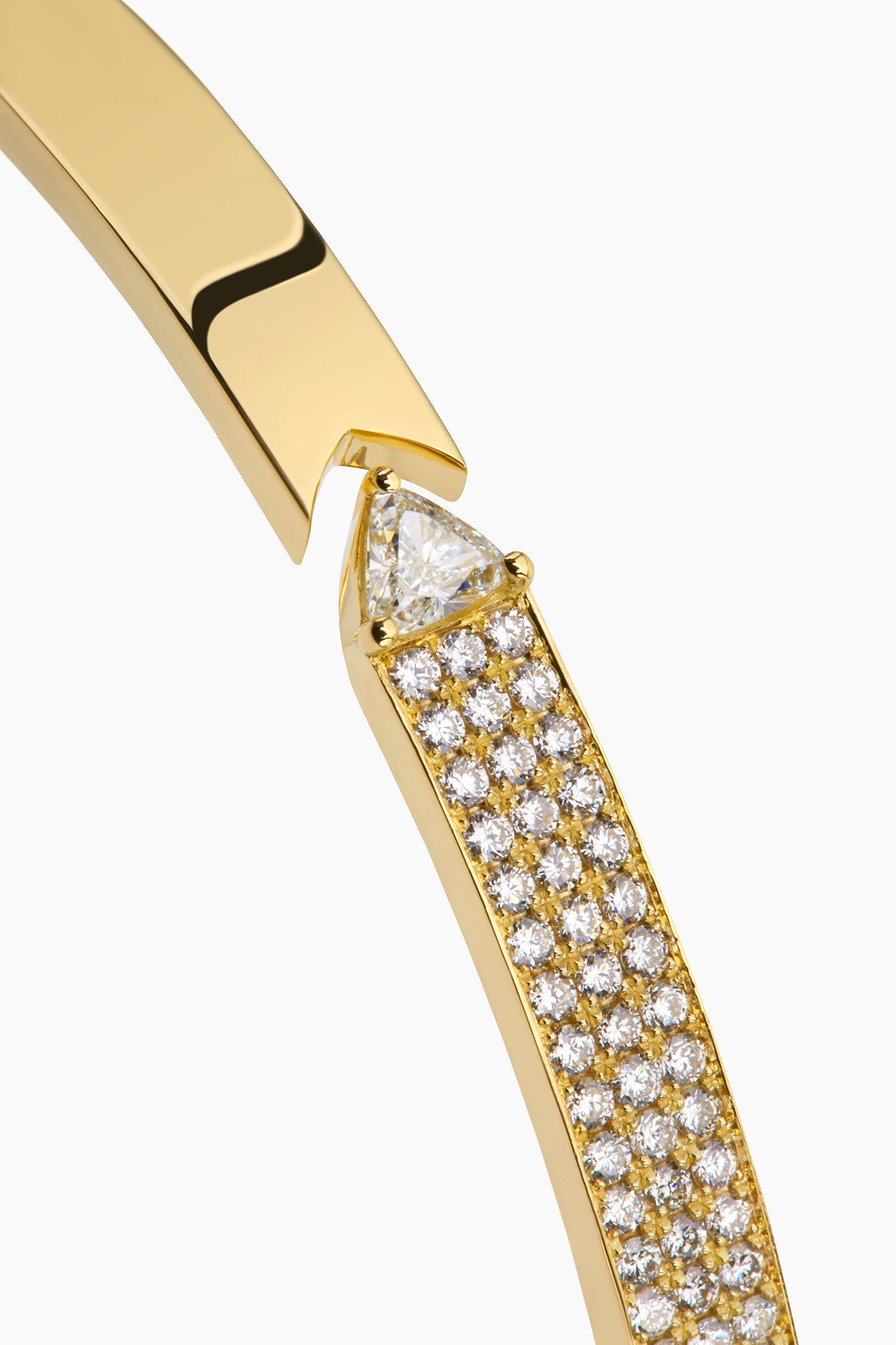 Close up of yellow gold bangle with round brilliant diamonds and trillion displayed against an off white background.