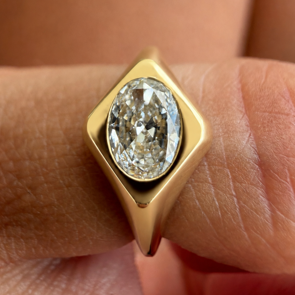 A close-up of a gold ring with a large oval clear gemstone, worn on a finger.