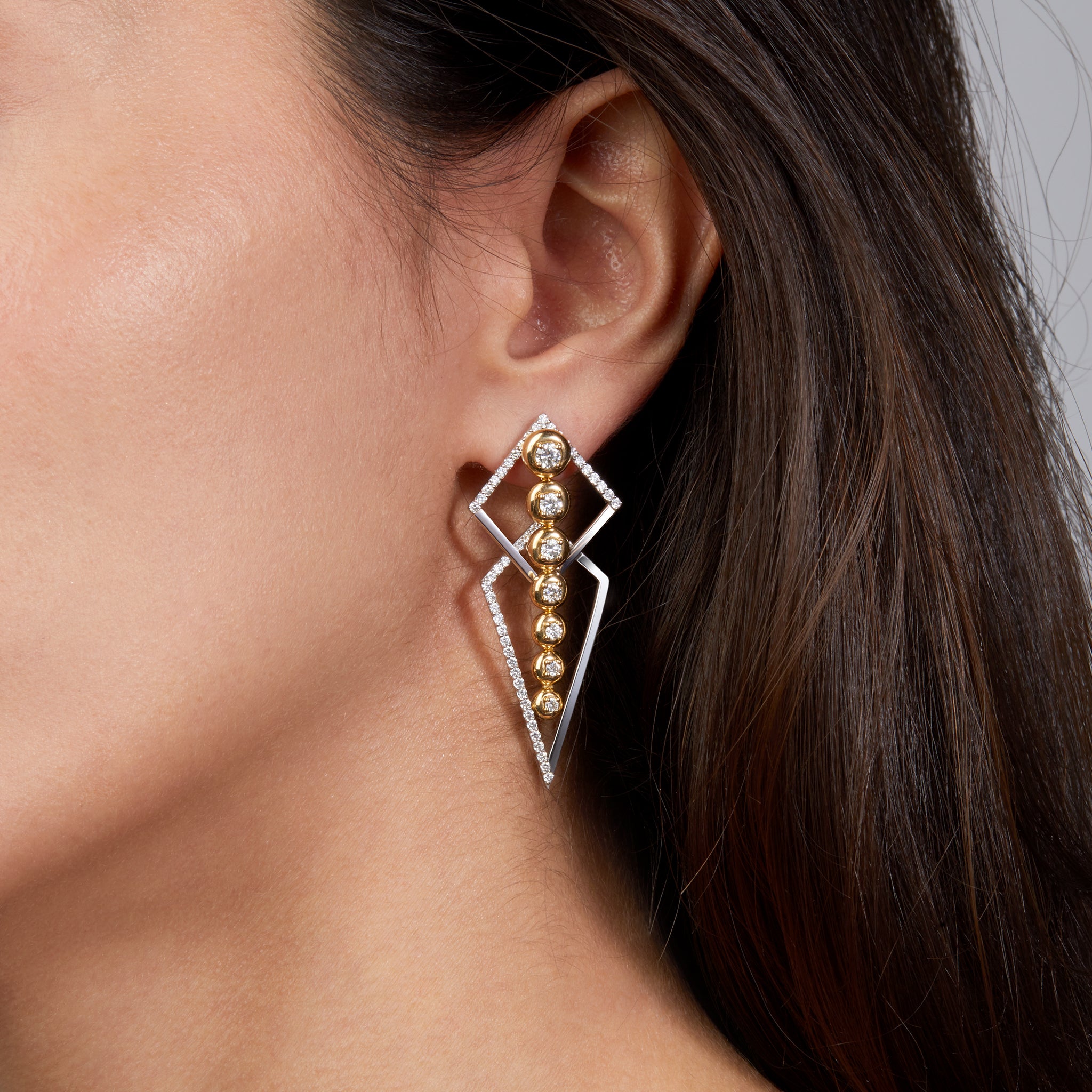 Two earrings combined in one in yellow and white gold displayed on model. 