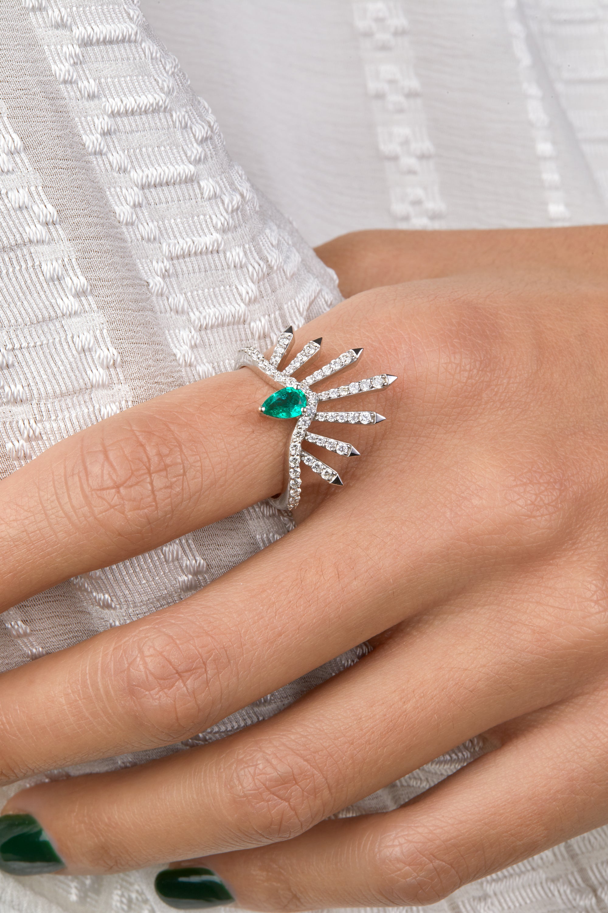 Diamond white gold ring with a pear shaped emerald portrayed facing each other on hand model wearing a denim jumpsuit.