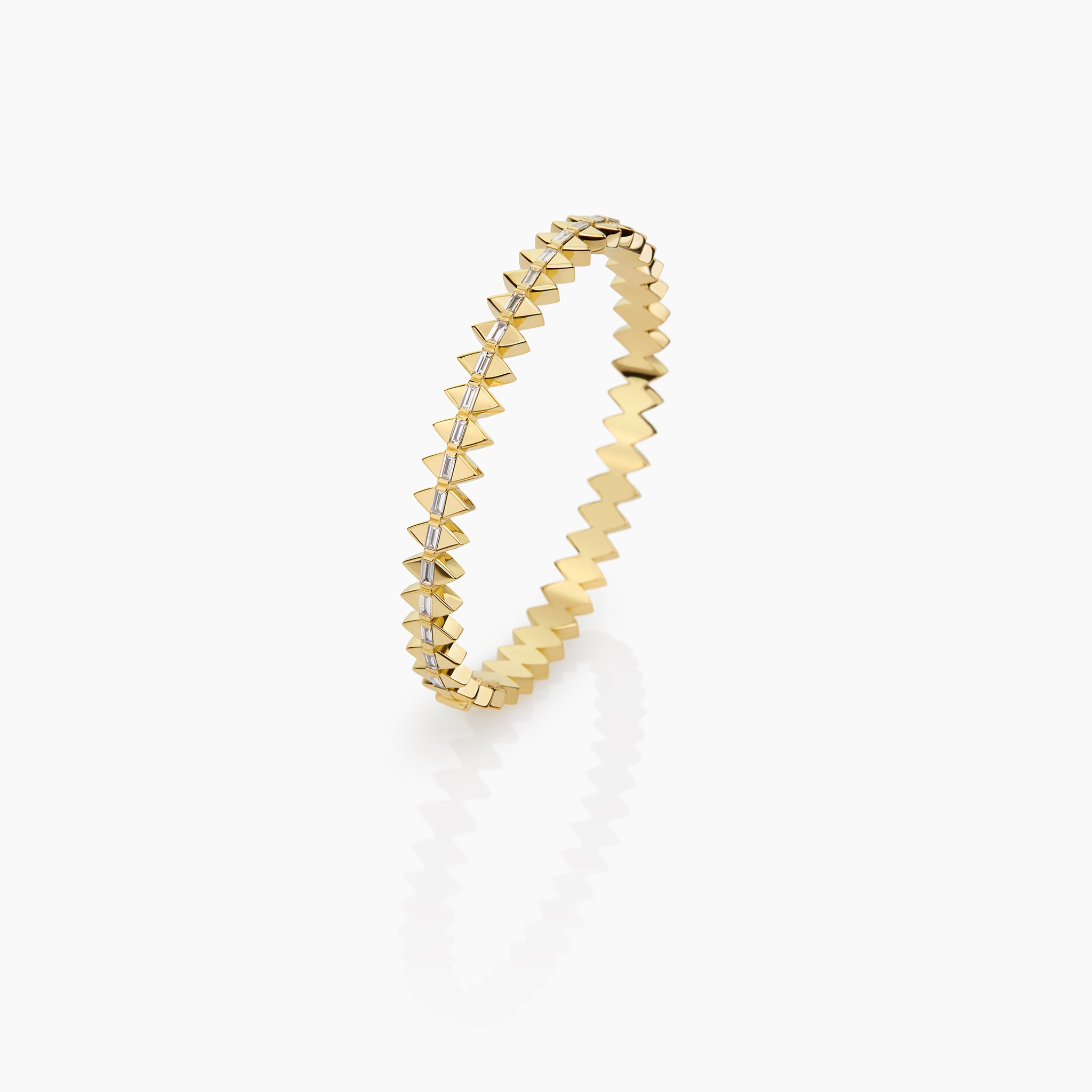 Solidarity bangle in yellow gold featuring diamond baguettes displayed against an off white background. 