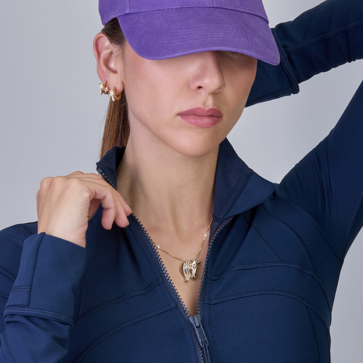 A model wearing a gold pendant necklace against a solid gray background.
