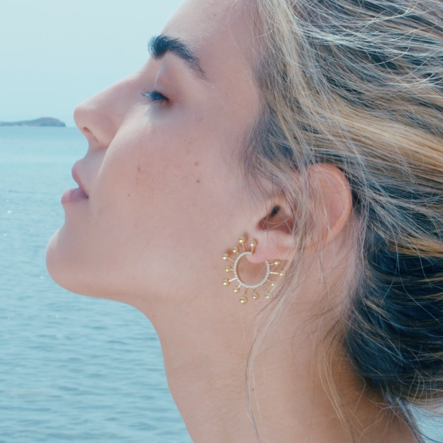 Yellow gold earrings elegantly worn by a model with a serene sea background.