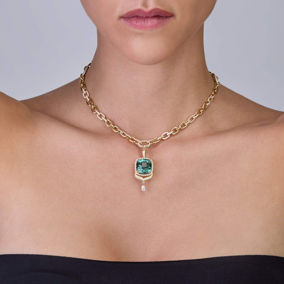 A close-up of a model wearing a gold chain necklace with a tourmaline pendant.