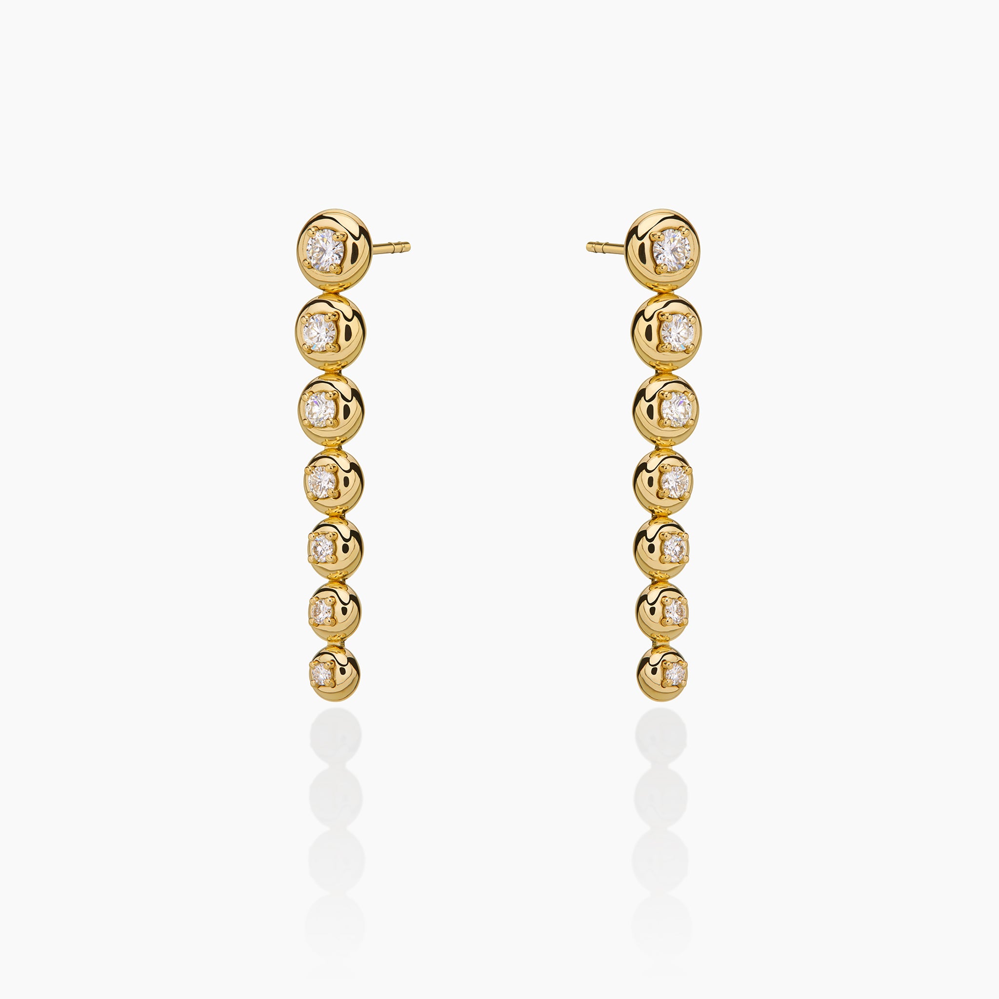 Star trail earrings in yellow gold adorned with diamonds displayed on an off white background. 