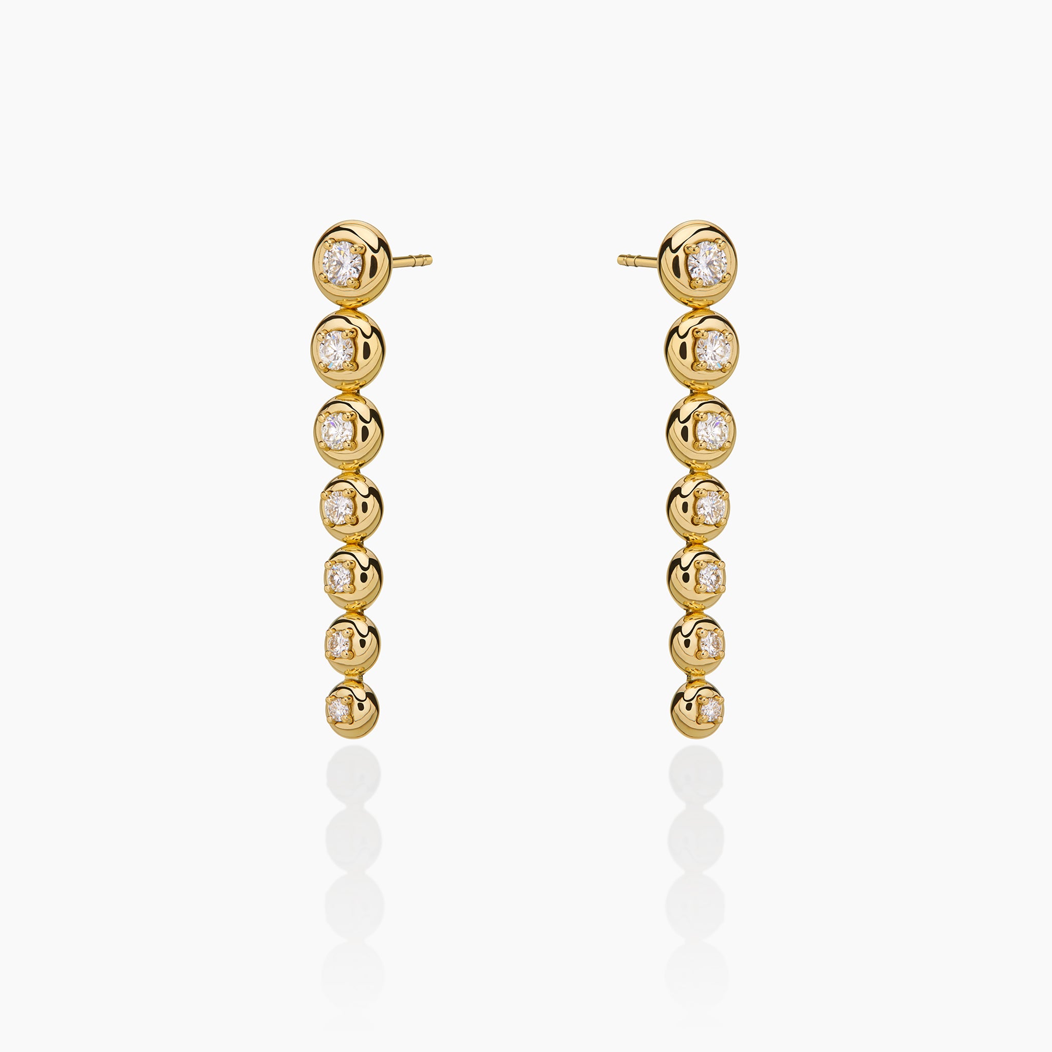 Star trail earrings in yellow gold adorned with diamonds displayed on an off white background. 