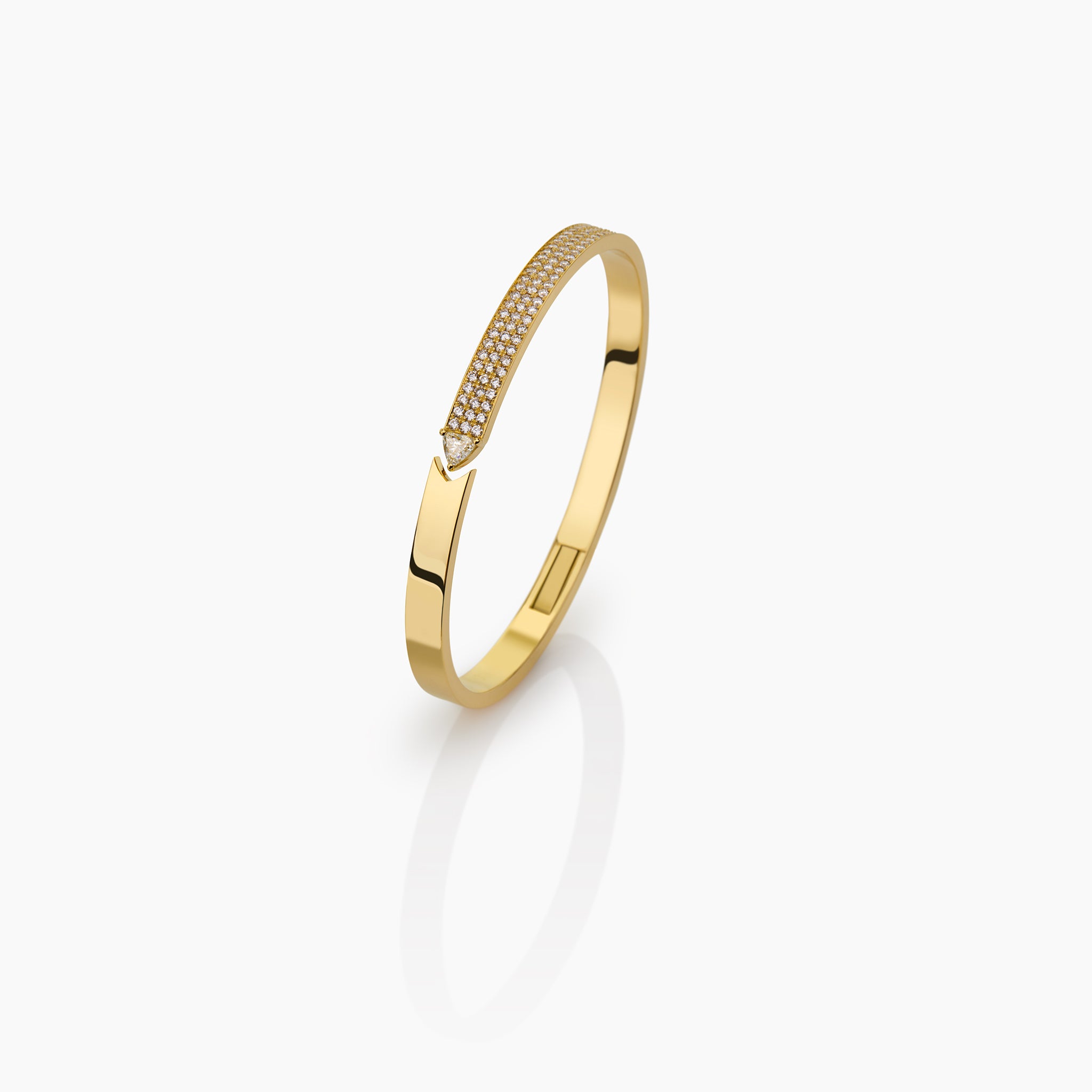 yellow gold bangle with round brilliant diamonds and trillion displayed against an off white background. 