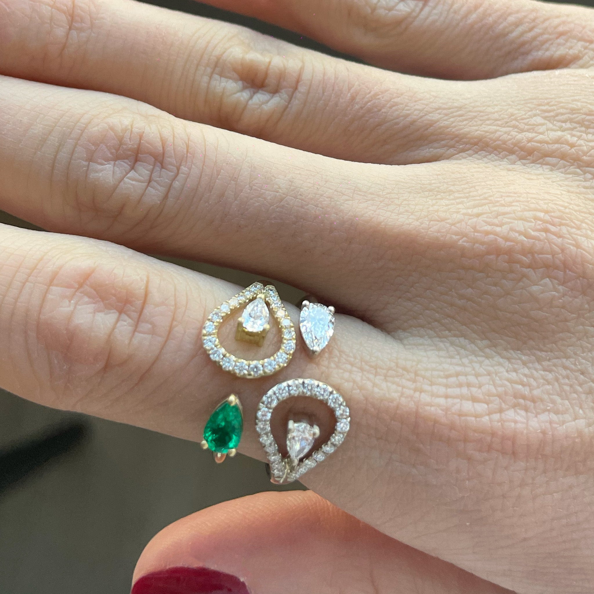 Two stunning rings  of the same design adorned with a vibrant single emerald stone and diamonds and a full diamond displayed on a hand model. 
