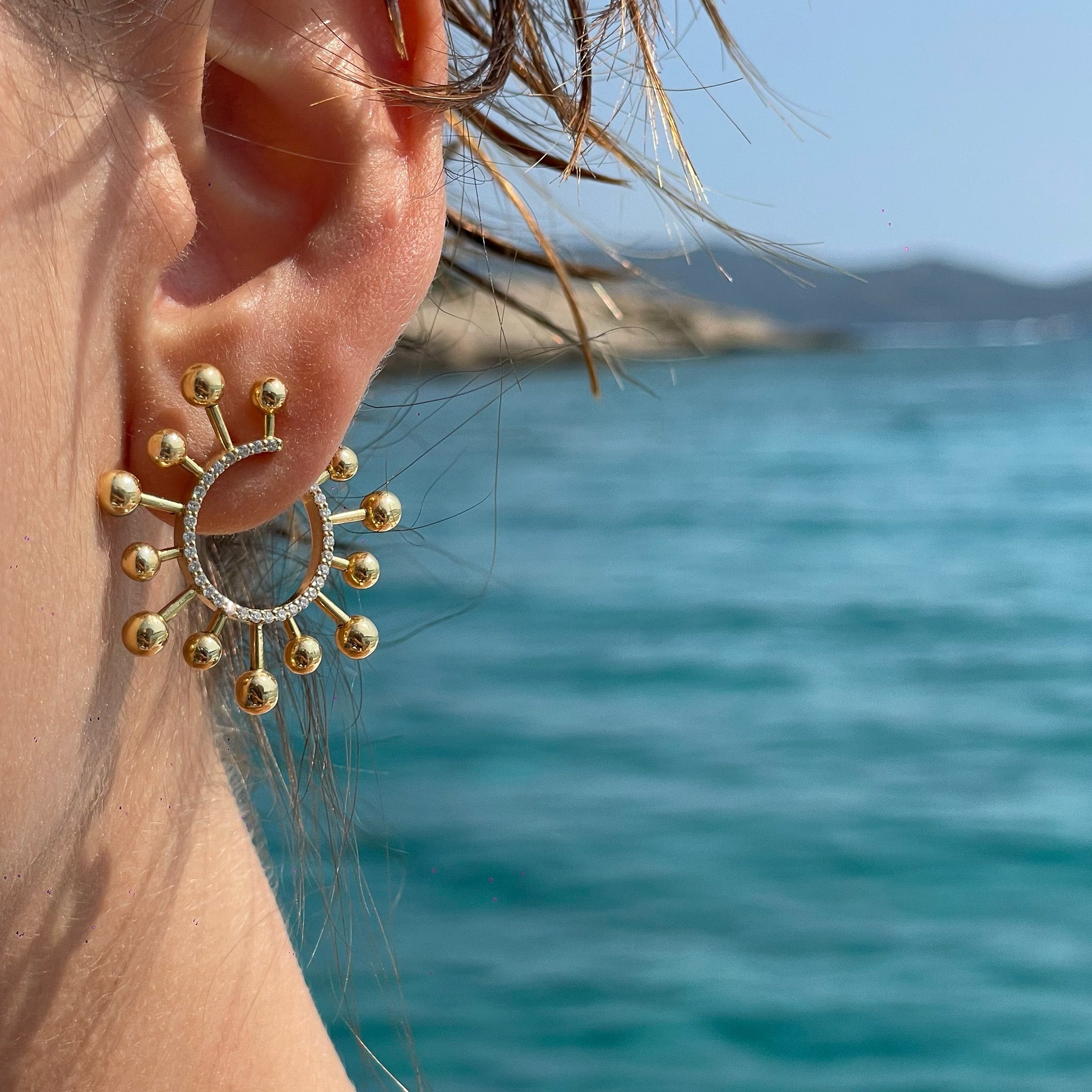 Yellow gold earrings elegantly worn by a model with a serene sea background.