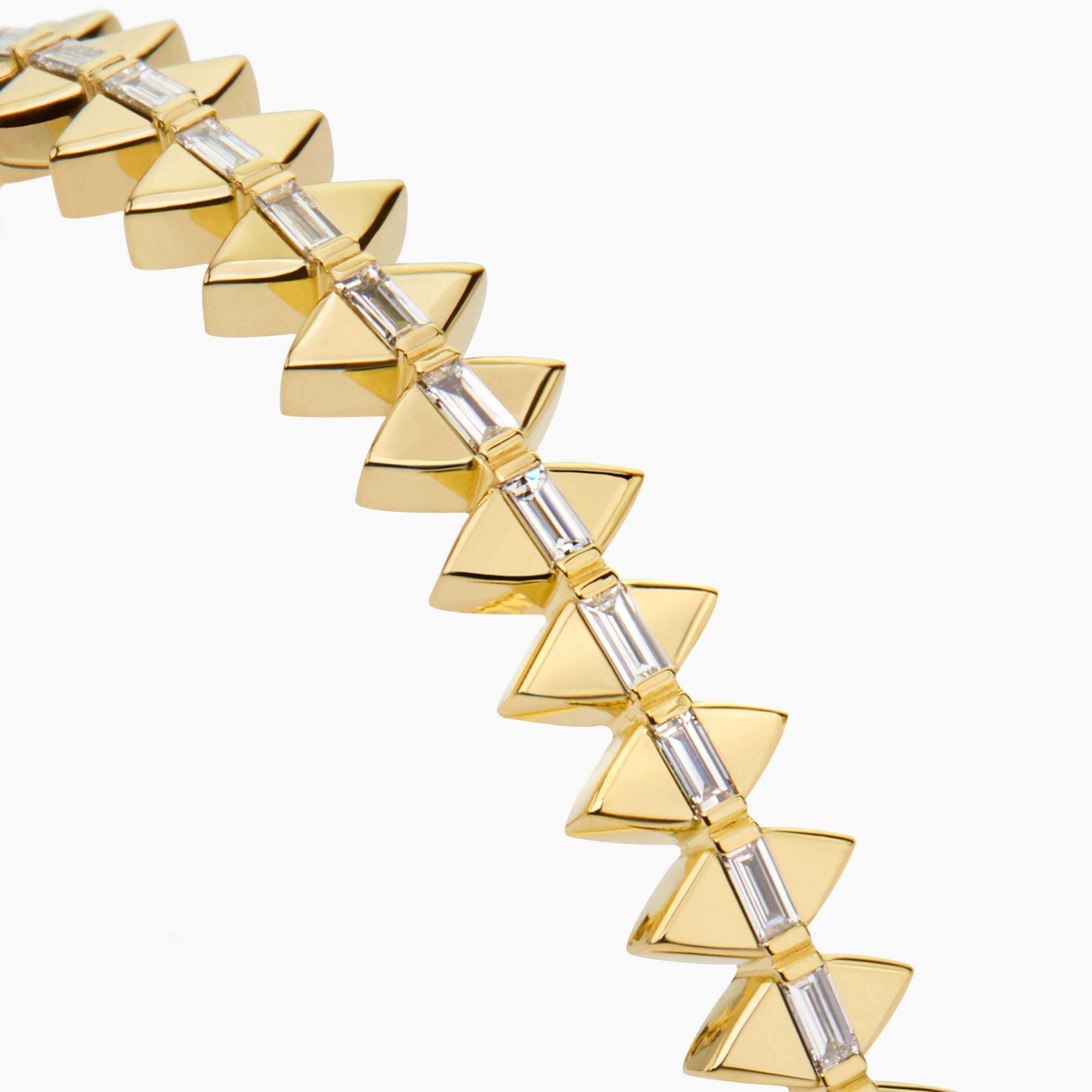 Solidarity bangle close up in yellow gold featuring diamond baguettes displayed against an off white background. 