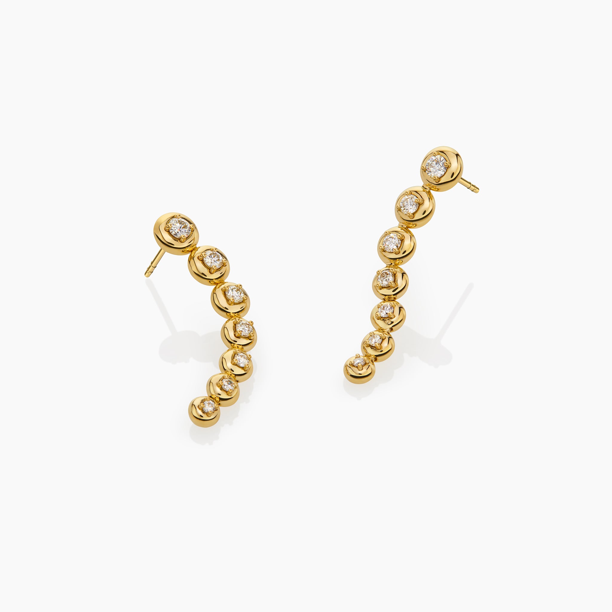Star trail earrings in yellow gold adorned with diamonds displayed on an off white background. 